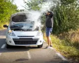 Mężczyzna z rozpaczą w rękach przy samochodzie z dymiącym silnikiem. Rozbiegany diesel na poboczu drogi.