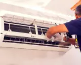 Un technicien en gants blancs effectue le nettoyage de climatisation, ouvrant l'unité pour accéder aux composants internes.