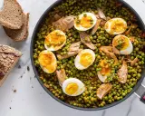 A skillet of peas and tuna with sliced hard-boiled eggs, served with bread.