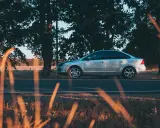 Srebrny sedan na tle drzew i pola. Ubezpieczenie auta zapewnia spokój ducha, a jego gwarantowana suma ubezpieczenia chroni przed nieprzewidzianymi wydatkami.