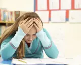 Verzweifeltes Mädchen mit Händen am Kopf im Klassenzimmer. Die **Kollektivstrafe Schule** lastet schwer auf ihr.