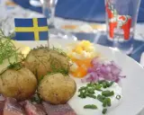 En klassisk midsommar meny med sill, färskpotatis, ägg, rödlök och gräddfil. En svensk flagga vajar stolt.