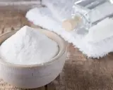 Soda oczyszczona w miseczce, obok ręcznik, buteleczka i szczoteczka. Czy soda oczyszczona odbarwia ubrania?