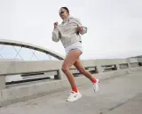 Läuferin mit hoher Kadenz auf einer Brücke, in Bewegung, mit Sonnenbrille und sportlicher Kleidung.