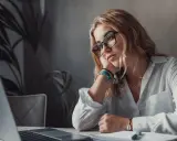 Zamyślona kobieta przy laptopie, z podpartą głową na dłoni. Wokół niej panuje atmosfera rezygnacji, jakby mówiła sobie: "nie mam marzeń".