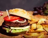 Burger maison avec pain aux graines, tomate, oignon, fromage et salade. Accompagné de frites. Une recette pain burger sans gluten à essayer !