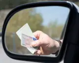 Mano sujetando un carnet de conducir y un documento de identidad reflejados en el espejo retrovisor de un coche.