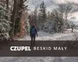 Kobieta w zimowej czapce i plecaku idzie zasypaną śniegiem trasą na Czupeł w Beskidzie Małym.