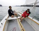 Deux personnes profitent d'une journée ensoleillée sur un voilier dayboat, naviguant sur une mer calme.