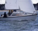 Voilier blanc naviguant sur une mer agitée, avec deux personnes à bord. Les premiers 18 avis sur ce modèle de bateau sont positifs.