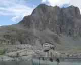 Rifugio sul lago della Vacca, con imponente parete rocciosa alle spalle.