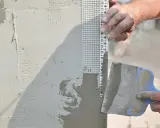 Tynkowanie narożnika z siatką zbrojącą, która chroni ścianę przed deszczem i pęknięciami.