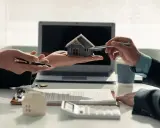 Deux mains présentent une maquette de maison, symbolisant comment devenir investisseur immobilier. Un contrat et un ordinateur sont visibles.