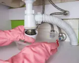 Mains de nettoyage rose démontant le siphon de lavabo bouché. Schéma montage siphon lavabo.