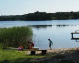 Dzieci szykują kajak nad spokojnym jeziorem w gminie Morąg. W tle las i drewniane molo.