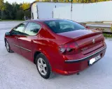 Błyszczący czerwony Peugeot 407 2.0 HDI z przyciemnianymi szybami stoi na żwirowym podjeździe.