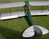 Ein detailgetreues Tiger Moth RC-Modellflugzeug mit silbernen Flügeln und grünem Rumpf steht auf einer grünen Wiese.