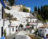 Weiße Häuser und Terrassen im Sacromonte, Granada, mit Kopfsteinpflaster und blühenden Pflanzen.