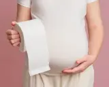 Brzuch kobiety w ciąży, trzymającej rolkę papieru toaletowego. Niestety, biegunka w ciąży to częsty problem.