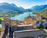 Borgo medievale con torre e lago turchese, incastonato tra i monti dell'Abruzzo.