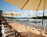 Väl dukade bord på en restaurang vid havet med segelbåtar i bakgrunden.