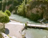 Las pozas de Horcajo de la Sierra ofrecen un refrescante baño en un entorno natural con puente, tobogán y gente disfrutando del agua y la arena.