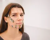 Kobieta z kolorowymi plastrami na twarzy, stosuje taping twarzy dla poprawy wyglądu.