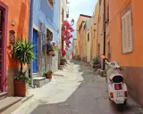 Un vicolo colorato con case arancioni e blu, fiori rossi e una Vespa bianca. Perfetto per le tue idee weekend nord Italia.
