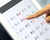 Palec wskazuje odpowiedź B na ekranie tabletu, gdzie trwa test baltimorski. Zaznaczone są już odpowiedzi B i C.