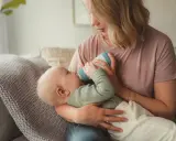 Mutter füttert Baby mit Flasche. Das Baby trinkt langsam, um die Verdauung zu unterstützen.