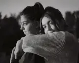 Dos mujeres se abrazan, una mirando al horizonte con **miedo al abandono**, la otra la abraza con ternura.