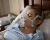 Kobieta śpi w masce CPAP, która zapewnia wspomaganie oddychania w domu. Urządzenie pomaga jej spokojnie przesypiać noce.