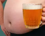 Ein Bierbauch, der zeigt, dass Bier dick macht. Eine Hand hält ein Glas Bier vor dem Bauch.