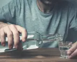 Mężczyzna nalewa alkohol do kieliszka. Nadmierne spożycie alkoholu negatywnie wpływa na żyły, prowadząc do ich uszkodzenia.
