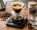 Ein detailliertes Kaffee-Rezept: Kaffeebohnen, gemahlener Kaffee, Wasser und ein Filter-Kaffeebereiter auf einer Waage.