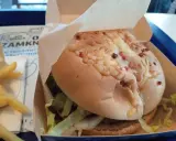 Pyszny burger drwala z chrupiącym bekonem i serem, w papierowym opakowaniu, obok porcji frytek.