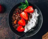 Schüssel mit Schokoladengranola, frischen Erdbeeren und cremigem Skyr oder Magerquark, garniert mit Minze.
