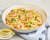 Eine Schüssel mit Spaghetti mit Garnelen, garniert mit Petersilie und Chiliflocken. Dazu Zitronenspalten und eine Gabel.