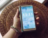 Dłoń trzyma telefon z wyświetloną godziną 11:11, co dla wielu ma szczególne znaczenie.