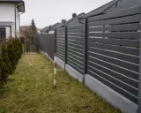 Nowoczesny, ciemnoszary płot oddziela posesje. Czy można postawić płot przy płocie sąsiada? Wąski pas trawy i żywopłot po lewej.