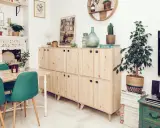 Muebles de madera clara con tiradores verdes, una mesa con sillas turquesas y una chimenea decorada. Inspiración para tu gama de colores para pintar muebles de madera.