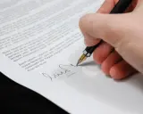 Dłoń podpisuje dokument piórem. Zastanawiasz się, jakie składki płaci emeryt od umowy zlecenia?