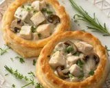 Deux vol-au-vent poulet crémeux, garnis de morceaux de poulet, de champignons et de persil frais, sur une assiette décorée.