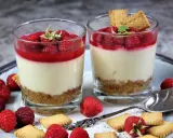 Zwei Gläser mit kalorienarmen Desserts im Glas: cremige Schicht, Himbeersoße und Keksboden. Garniert mit frischen Himbeeren und Keksen.