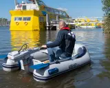Un homme pilote un bateau gonflable propulsé par la puissance d'un moteur électrique, naviguant près d'un grand bateau jaune.
