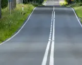 Droga wijąca się wśród zieleni, z podwójną białą **linią ciągłą** pośrodku.