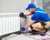 Un plombier effectue le branchement radiateur eau. Il installe un nouveau radiateur blanc sur un mur en béton.