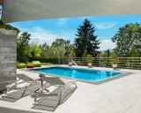 Moderne idee aiuole bordo piscina: piante in vaso e pouf colorati creano un'oasi rilassante.