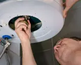 Main qui répare un chauffe-eau, une fuite d'eau s'échappe du cumulus qui fuit par le haut.
