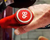Mano sujetando una boquilla de gasolina roja con el número 96, indicando uno de los tipos de gasolina en España.